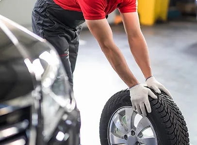 Mécanicien en gants blancs, penché, pousse un pneu de voiture à Nanterre en Hauts-de-Seine 92