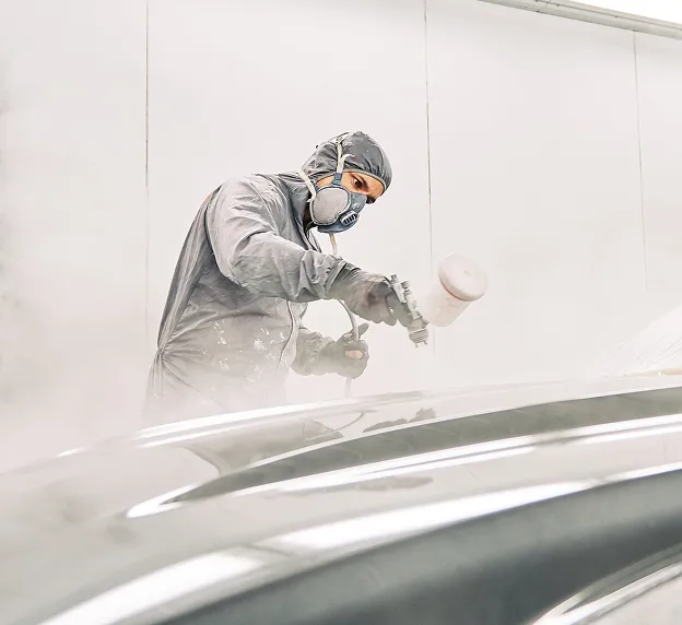 Peintre automobile en tenue de protection et masque, peignant une voiture à Nanterre en Hauts-de-Seine 92