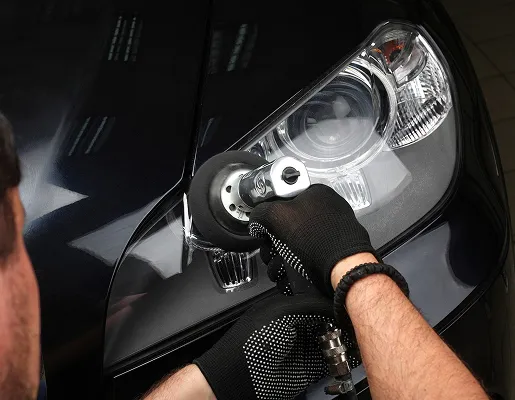 Une main gantée polit un phare de voiture noir avec une polisseuse à Nanterre en Hauts-de-Seine 92