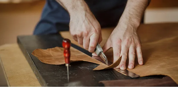 Mains coupant du cuir marron sur une planche de travail à Nanterre en Hauts-de-Seine 92u