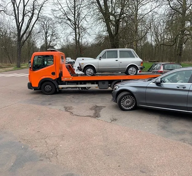 Dépanneuse orange transportant une voiture argentée, garée à côté d'une berline grise à Nanterre en Hauts-de-Seine 92